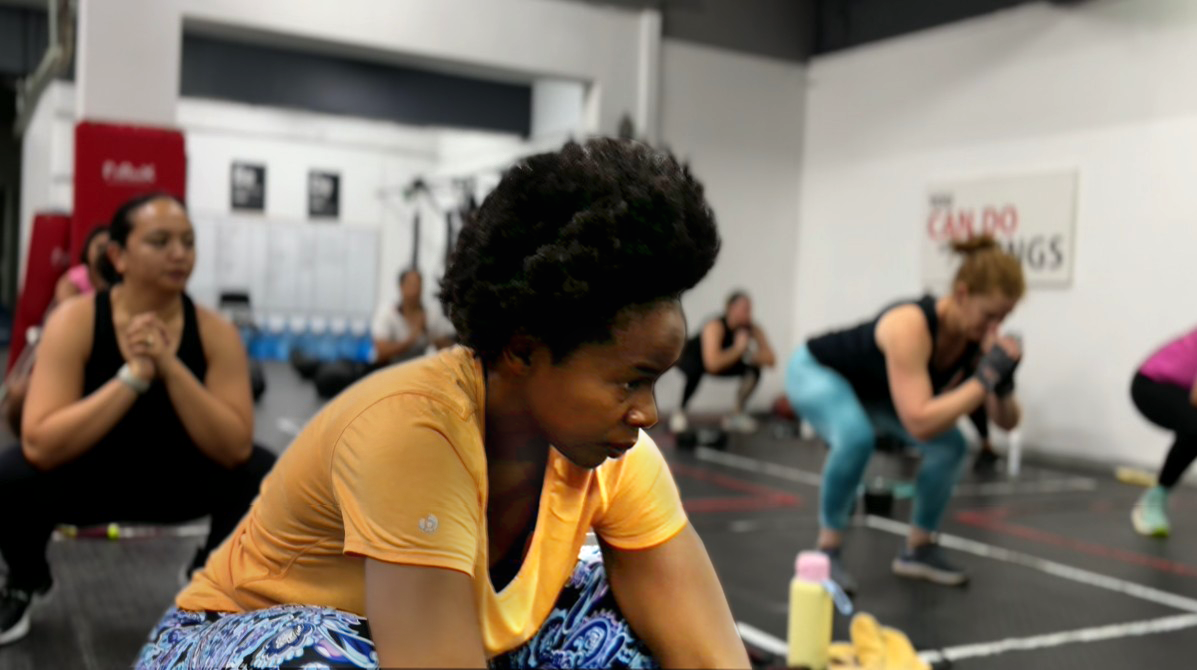 Strength and Focus in a FitRanX Functional Fitness Class A focused woman in a yellow shirt resting between sets during a functional fitness class at FitRanX, with other members in the background.