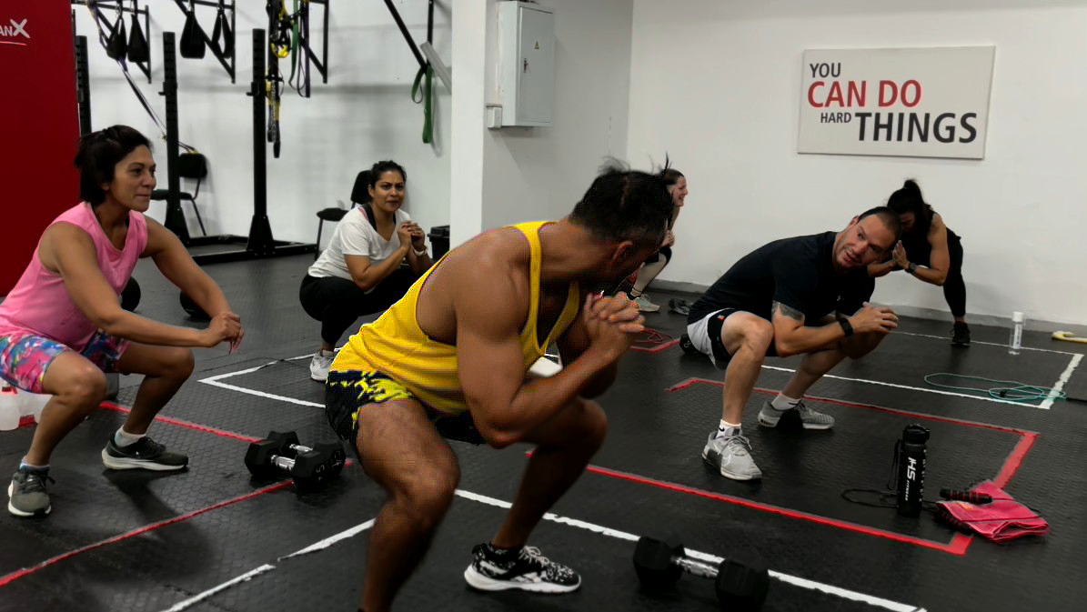 FitRanX Functional Fitness: Mastering the Squat A group of diverse athletes performing squats in a FitRanX functional fitness gym, with dumbbells on the floor.