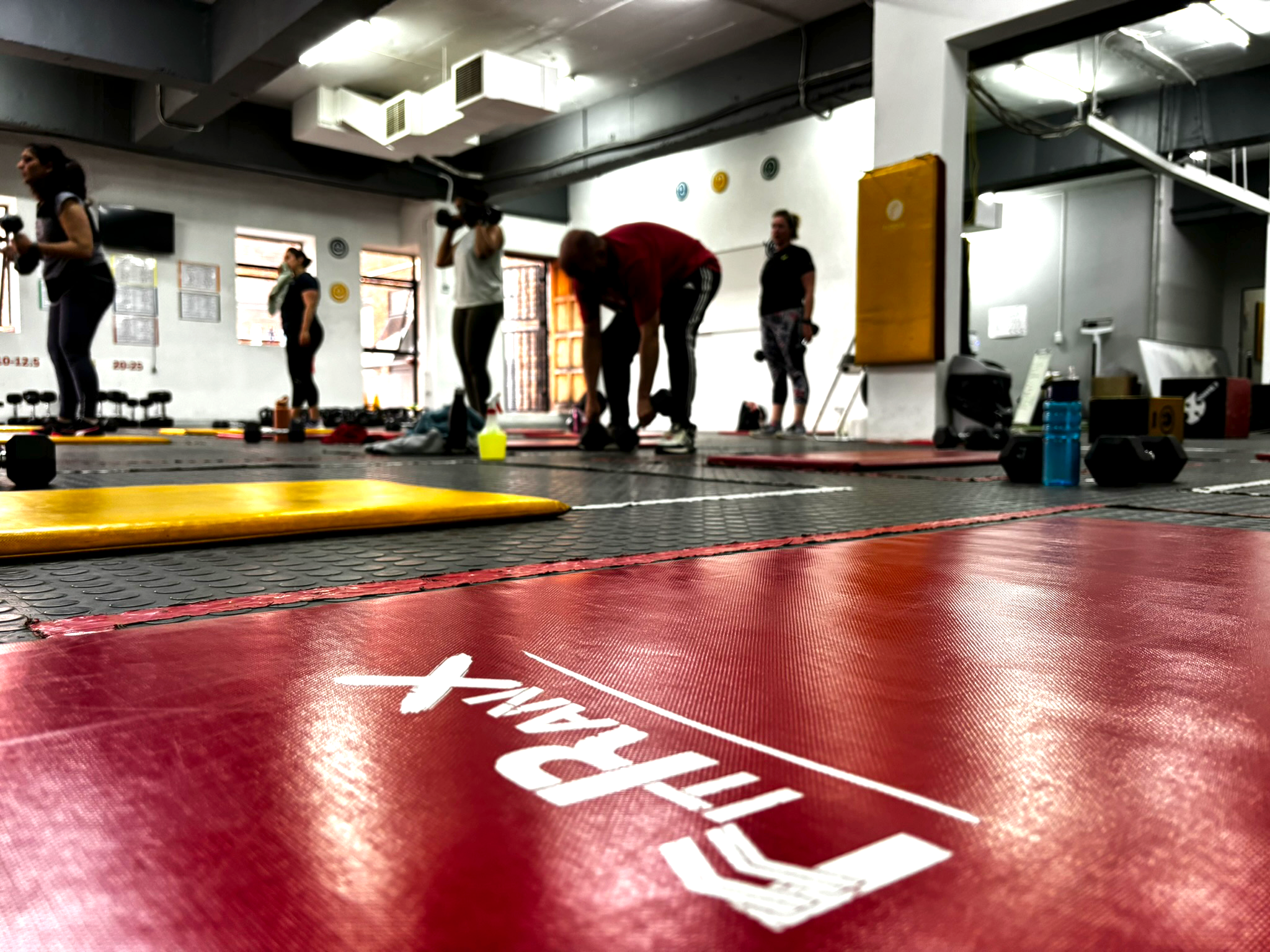 A low-angle shot of the FitRanX logo on the gym floor with a group of people training in the background.